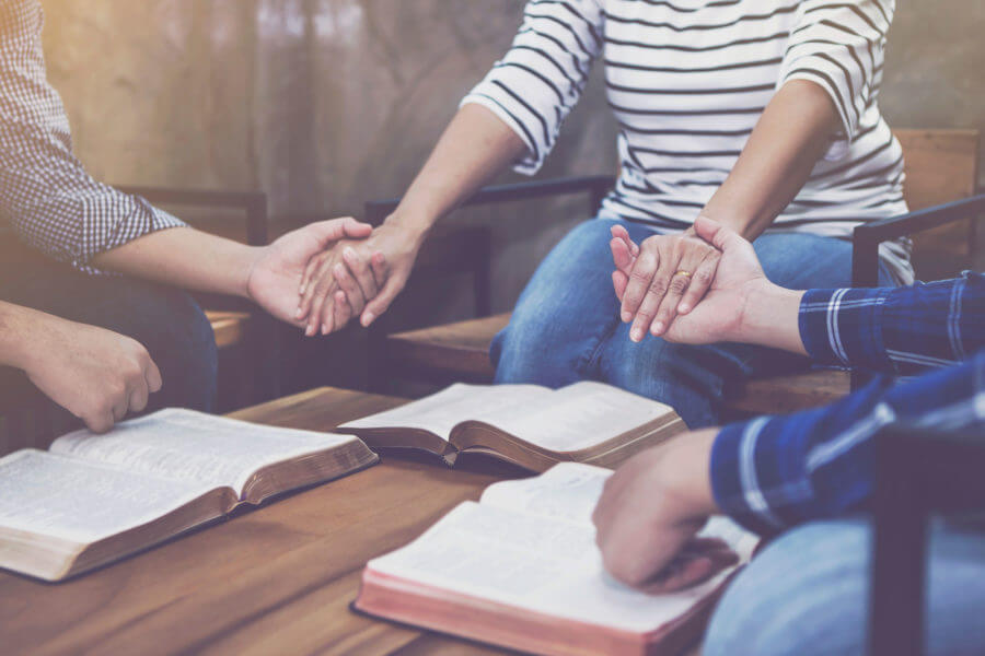 Prayer Group holding hands bibles